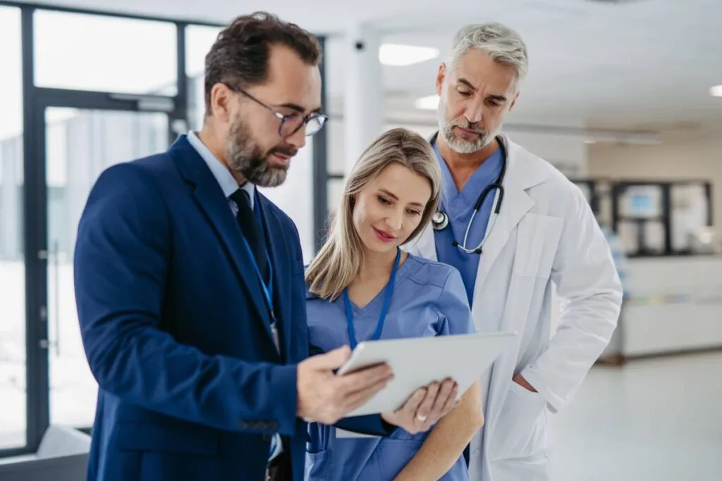 An administrator holding a tablet and talking to two doctors