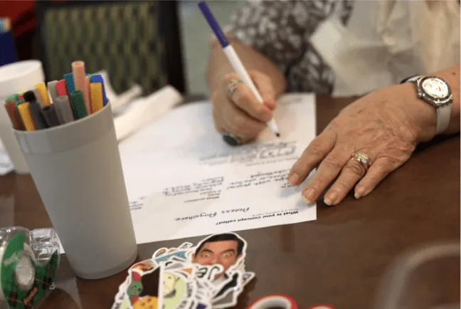 Participant writing responses on a workshop worksheet at a table of markers