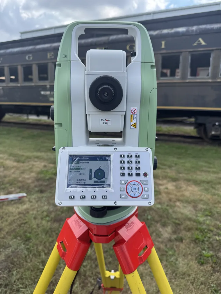 A Leica Geosystems Total Station on a tripod in front of a vintage rail car during a field measurement session